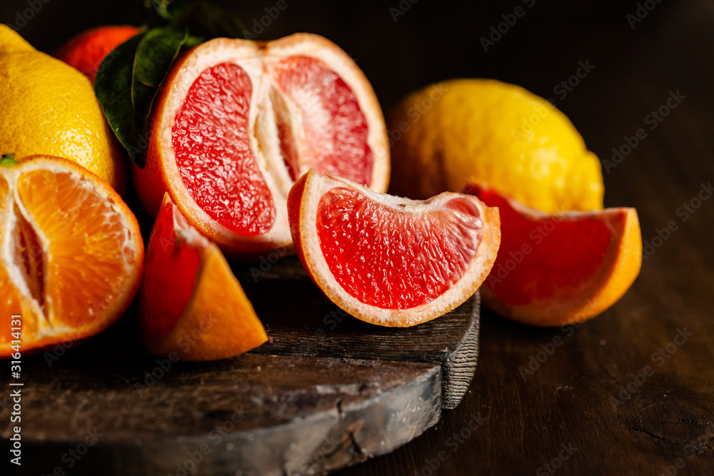 Slices of ripe fresh organic citrus fruits: grapefruit, orange, lemon on wooden board. Natural source of vitamins, low calories tasty dessert. Dark background, close up, front view Slices of ripe fresh organic citrus fruits: grapefruit, orange, lemon on wooden board. Natural source of vitamins, low calories tasty dessert. Dark background, close up, front view