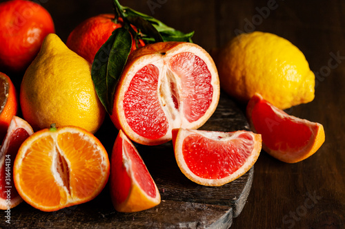 Slices of ripe fresh organic citrus fruits: grapefruit, orange, lemon on wooden board. Natural source of vitamins, low calories tasty dessert. Dark background, close up, front view