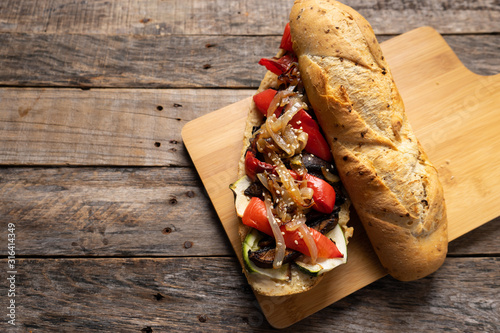 Vegan sub sandwich with grilled vegetables on wooden background