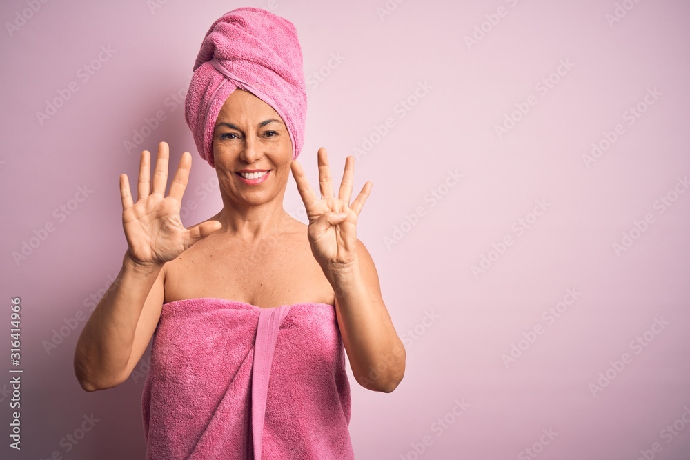 Middle age woman wearing bath towel from beauty body care over pink background showing and pointing up with fingers number nine while smiling confident and happy. Middle age woman wearing bath towel from beauty body care over pink background showing and pointing up with fingers number nine while smiling confident and happy.