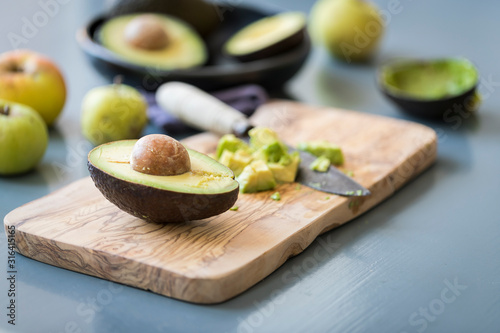 avocado cut in half on a wooden cutting board with chopped avocado 's , wooden knife 