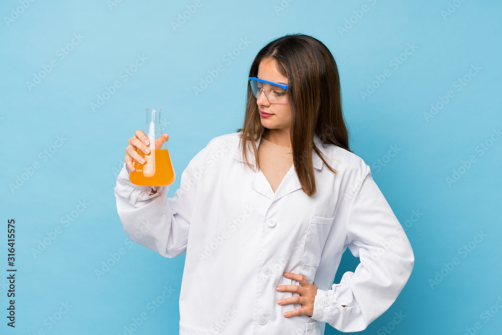 Young brunette girl over isolated blue background with a scientific test tube Young brunette girl over isolated blue background with a scientific test tube