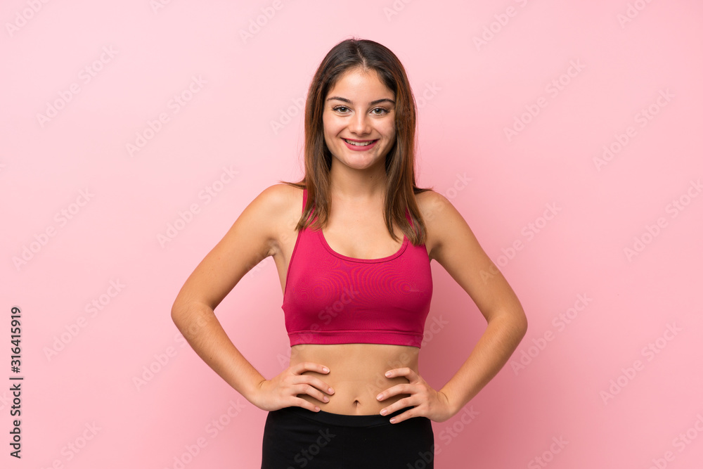 Young sport girl over isolated pink background posing with arms at hip and smiling