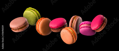Flying french colorful macaroons on wooden table isolated on black