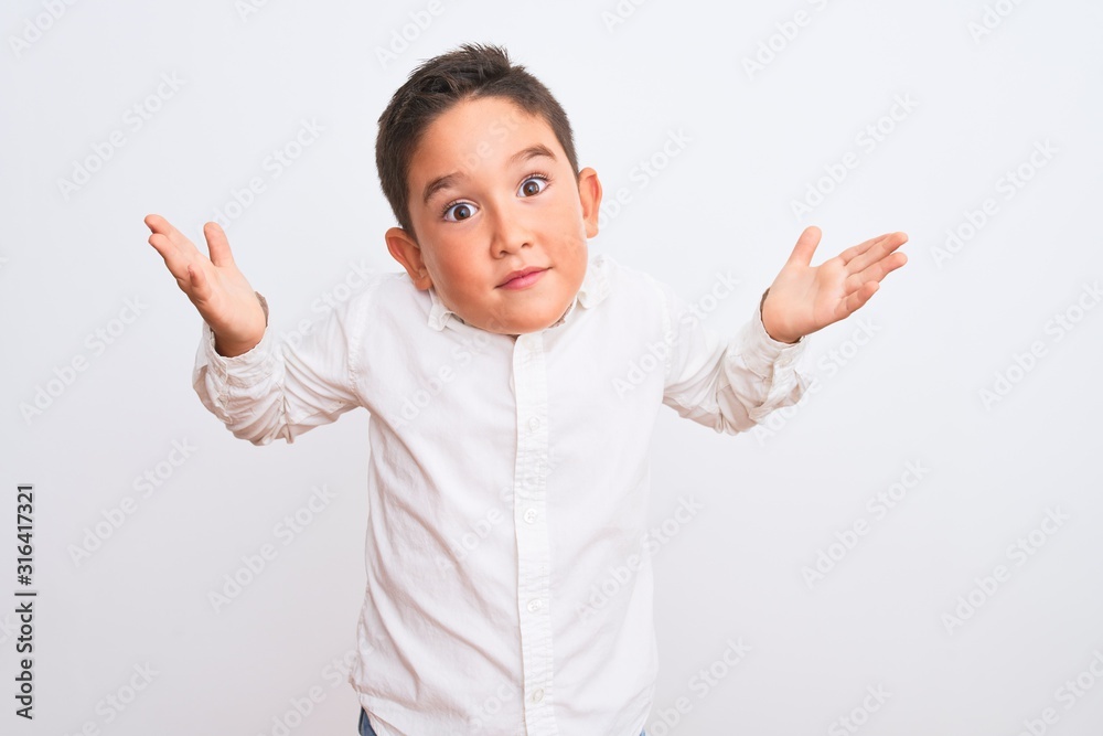 Beautiful kid boy wearing elegant shirt standing over isolated white background clueless and confused expression with arms and hands raised. Doubt concept.
