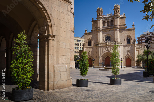View of the Main square of Castellón de la Plana with the Co-Cathedral of Santa Maria in the background and the arcades of the city council building on a sunny day with a blue sky, Spain photo