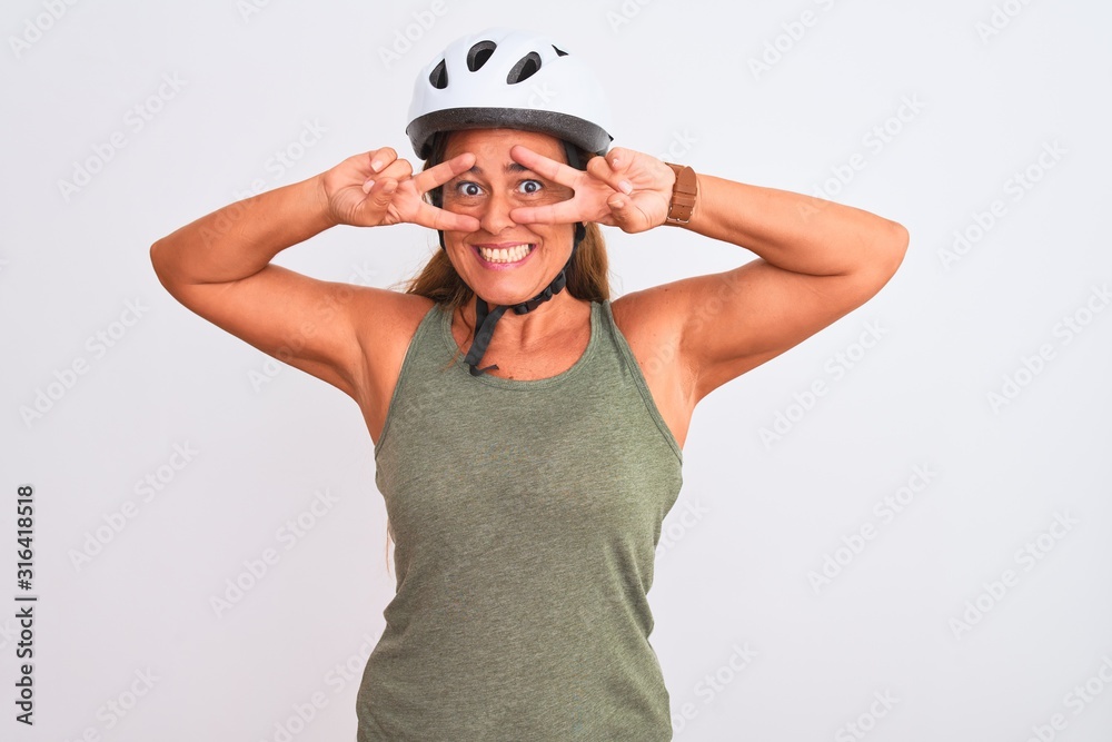 Middle age mature cyclist woman wearing safety helmet over isolated background Doing peace symbol with fingers over face, smiling cheerful showing victory Middle age mature cyclist woman wearing safety helmet over isolated background Doing peace symbol with fingers over face, smiling cheerful showing victory