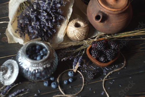 blueberries and blackberries in a vintage jar and wooden plate, lavender and dried flowers. vintage village style © Volha