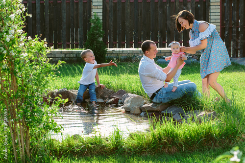 Cheerful family walking in the garden of a private house, playing on a sunlit blossoming fresh and juicy green lawn at pond