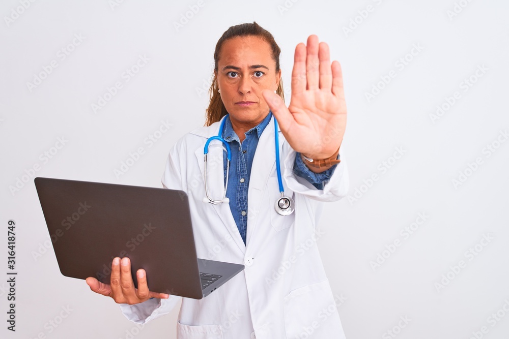 Middle age mature doctor woman holding computer laptop over isolated background with open hand doing stop sign with serious and confident expression, defense gesture Middle age mature doctor woman holding computer laptop over isolated background with open hand doing stop sign with serious and confident expression, defense gesture