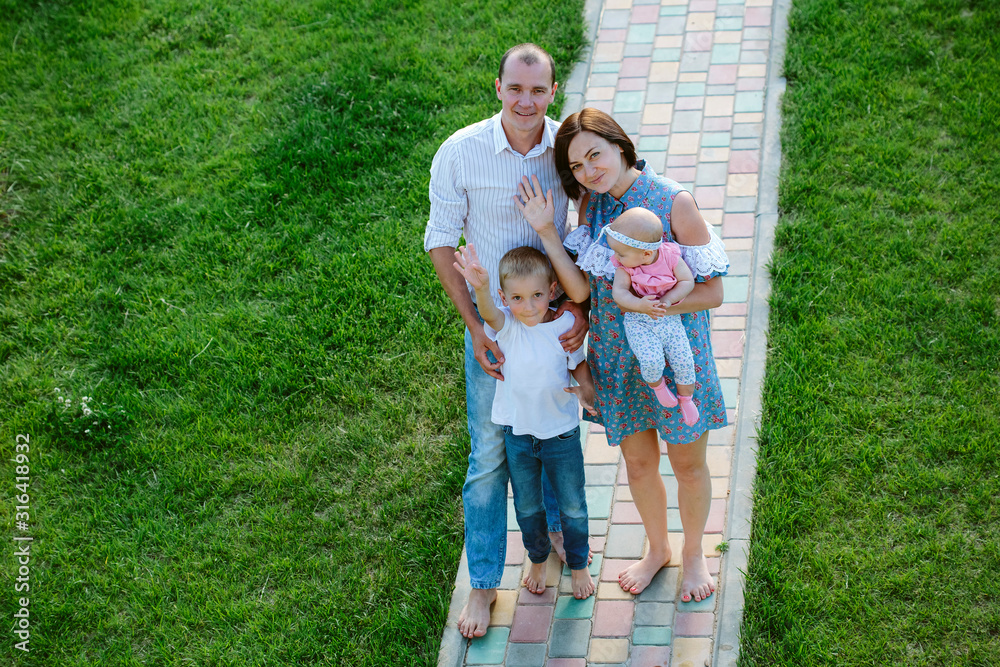Parents with children hugging happily on a green lawn and wave their hand at the camera Parents with children hugging happily on a green lawn and wave their hand at the camera