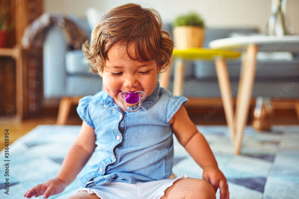 Beautiful toddler child girl wearing denim shirt sitting on the carpet using pacifier Beautiful toddler child girl wearing denim shirt sitting on the carpet using pacifier