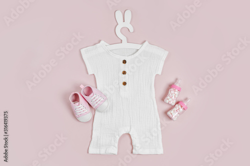 Set of baby clothes and accessories on pink background. White bodysuit on cute hanger with bunny ears and baby shoes and toys. Fashion newborn clothes. Flat lay, top view photo