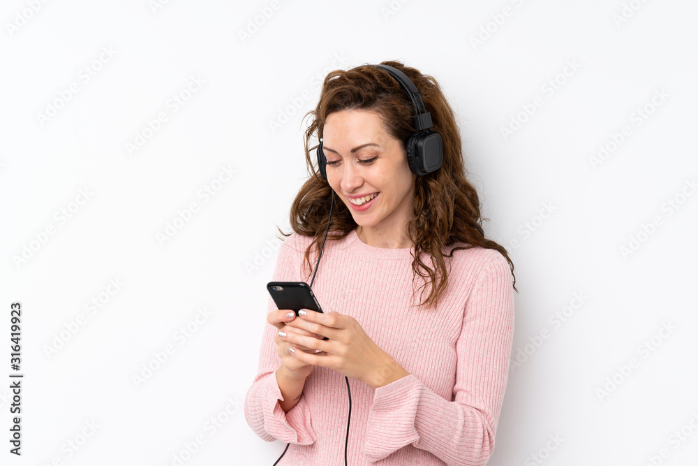 Young pretty woman over isolated background using the mobile with headphones Young pretty woman over isolated background using the mobile with headphones