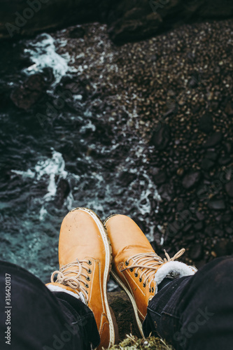 Traveler's brown boots against dark coast of Atlantic ocean in Iceland.