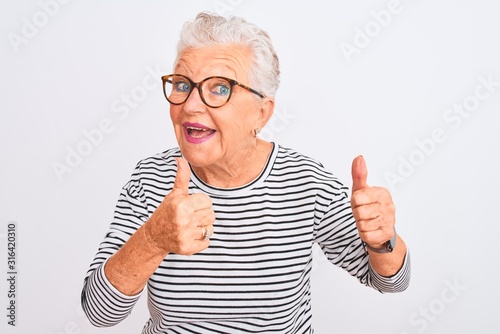Senior grey-haired woman wearing striped navy t-shirt glasses over isolated white background pointing fingers to camera with happy and funny face. Good energy and vibes.