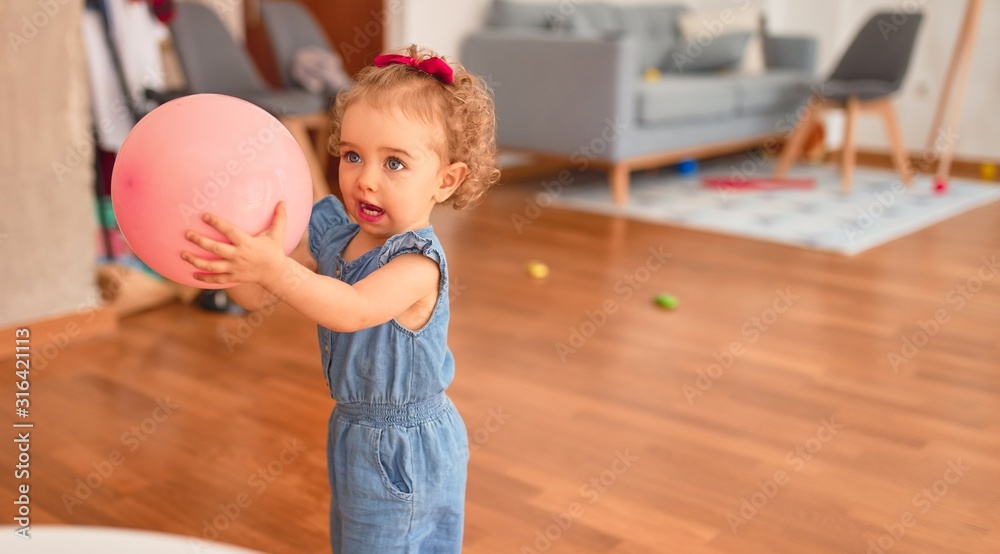 Fototapeta premium Beautiful caucasian infant playing with toys at colorful playroom. Happy and playful with pink baloon at kindergarten.
