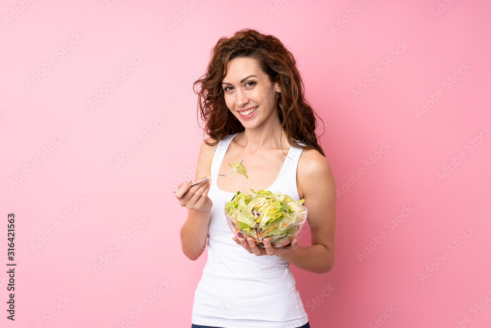 Young woman with curly hair holding a salad over isolated pink background Young woman with curly hair holding a salad over isolated pink background