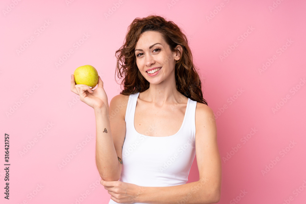 Young woman with curly hair holding an apple over isolated pink background Young woman with curly hair holding an apple over isolated pink background