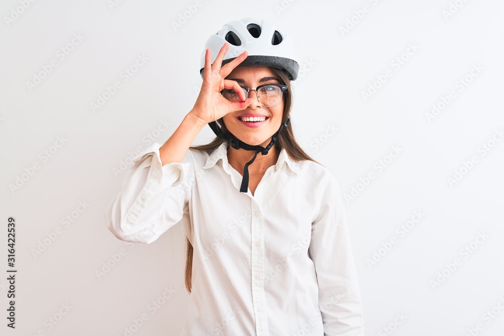 Beautiful businesswoman wearing glasses and bike helmet over isolated white background doing ok gesture with hand smiling, eye looking through fingers with happy face. Beautiful businesswoman wearing glasses and bike helmet over isolated white background doing ok gesture with hand smiling, eye looking through fingers with happy face.