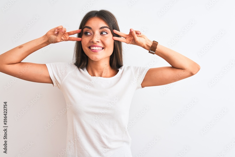 Young beautiful woman wearing casual t-shirt standing over isolated white background Doing peace symbol with fingers over face, smiling cheerful showing victory Young beautiful woman wearing casual t-shirt standing over isolated white background Doing peace symbol with fingers over face, smiling cheerful showing victory