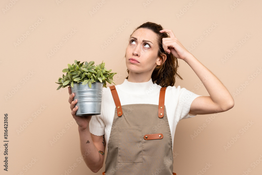 Gardener woman holding a plant having doubts and with confuse face expression Gardener woman holding a plant having doubts and with confuse face expression