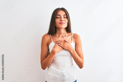 Young beautiful woman wearing casual t-shirt standing over isolated white background smiling with hands on chest with closed eyes and grateful gesture on face. Health concept. © Krakenimages.com