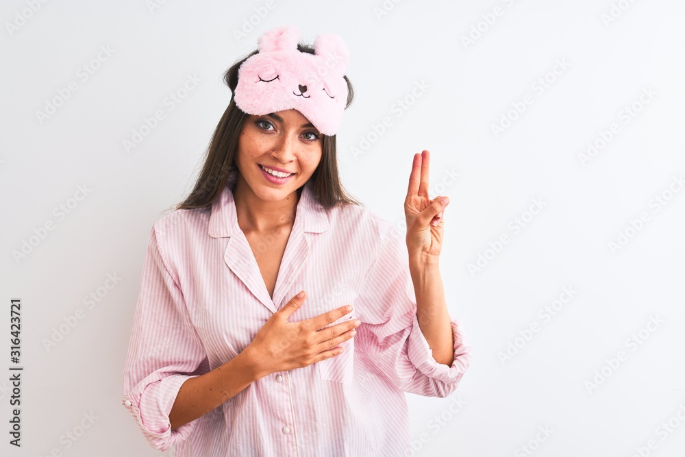 Young beautiful woman wearing sleep mask and pajama over isolated white background smiling swearing with hand on chest and fingers up, making a loyalty promise oath Young beautiful woman wearing sleep mask and pajama over isolated white background smiling swearing with hand on chest and fingers up, making a loyalty promise oath