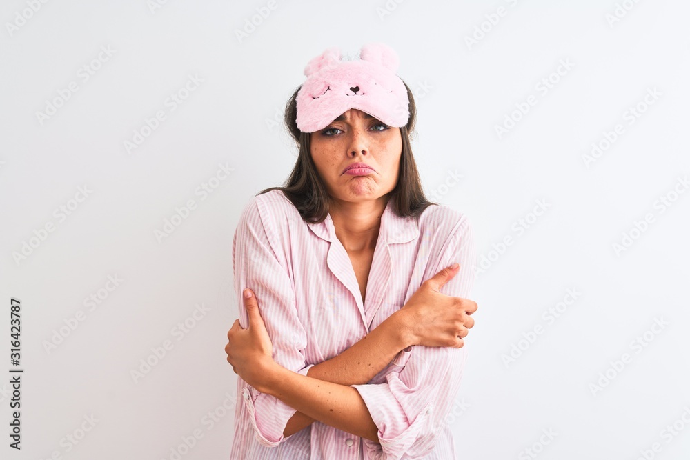 Young beautiful woman wearing sleep mask and pajama over isolated white background shaking and freezing for winter cold with sad and shock expression on face Young beautiful woman wearing sleep mask and pajama over isolated white background shaking and freezing for winter cold with sad and shock expression on face