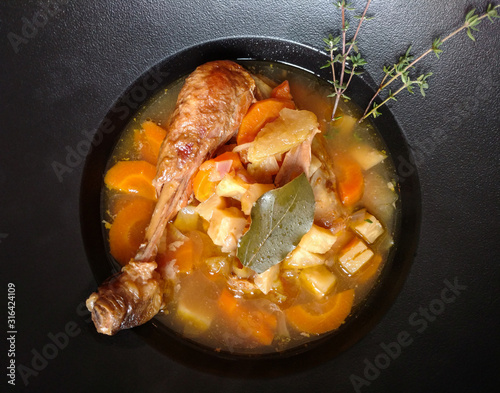 Vegetable soup with a chicken leg in the cast iron soup plate, top view