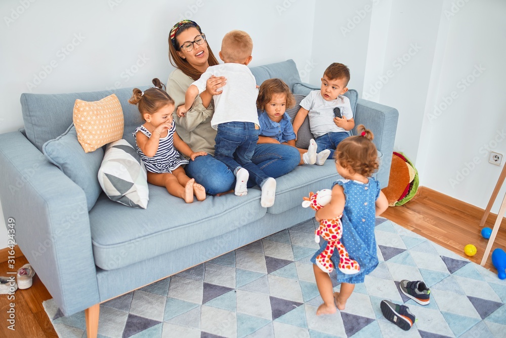 Beautiful teacher and group of toddlers sitting on the sofa playing at kindergarten