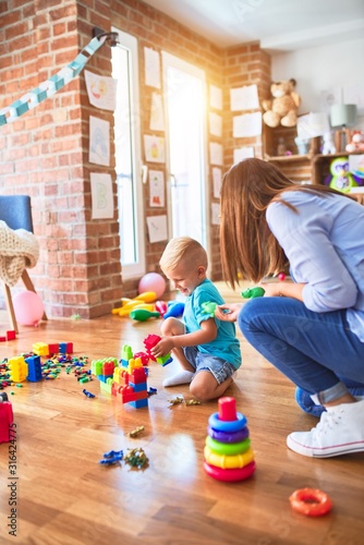 Young caucasian child playing at playschool with teacher. Mother and son at playroom around toys.