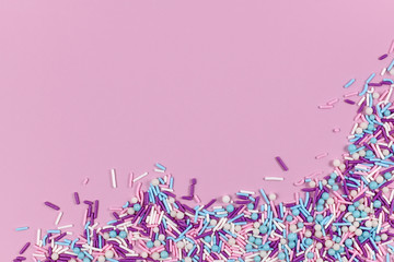 Colorful white, pink, blue and purple sugar sprinkles in shape of balls and sticks on pink background with blank copy space