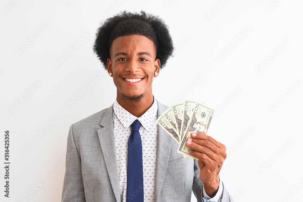 Young african american businessman holding dollars standing over isolated white background with a happy face standing and smiling with a confident smile showing teeth Young african american businessman holding dollars standing over isolated white background with a happy face standing and smiling with a confident smile showing teeth