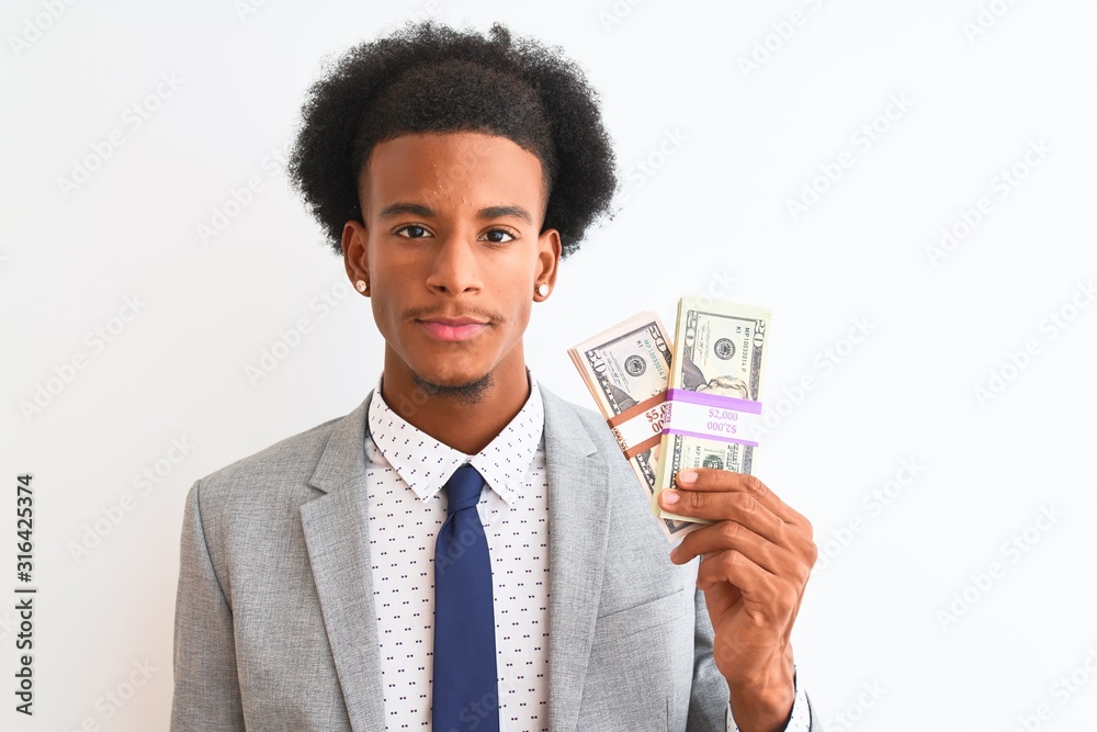 Young african american businessman holding dollars standing over isolated white background with a confident expression on smart face thinking serious Young african american businessman holding dollars standing over isolated white background with a confident expression on smart face thinking serious
