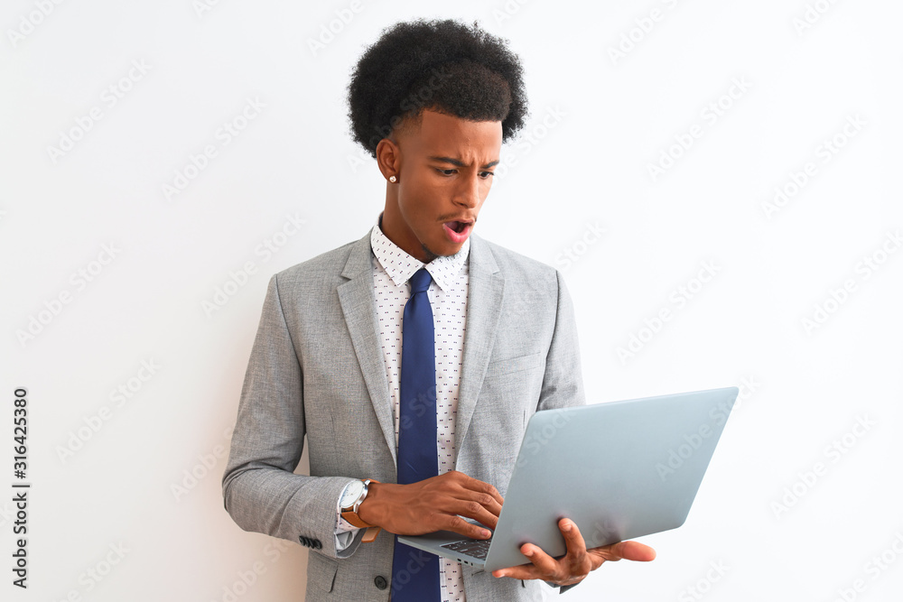 Young african american businessman using laptop standing over isolated white background scared in shock with a surprise face, afraid and excited with fear expression Young african american businessman using laptop standing over isolated white background scared in shock with a surprise face, afraid and excited with fear expression