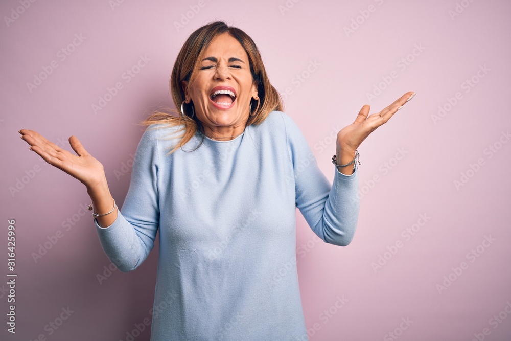 Middle age beautiful woman wearing casual t-shirt standing over isolated pink background celebrating mad and crazy for success with arms raised and closed eyes screaming excited. Winner concept Middle age beautiful woman wearing casual t-shirt standing over isolated pink background celebrating mad and crazy for success with arms raised and closed eyes screaming excited. Winner concept