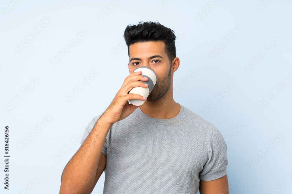 Young handsome man over isolated background holding and drinking a coffee to take away Young handsome man over isolated background holding and drinking a coffee to take away