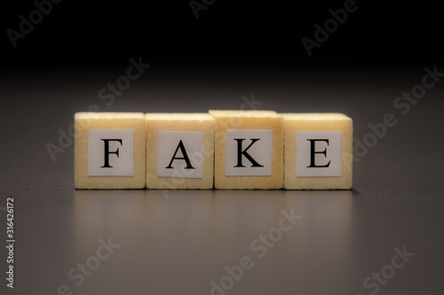 The word FAKE written on wooden cubes isolated on a black background