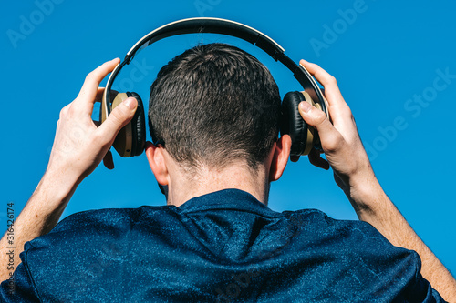 caucasian Young guy from back putting on music headphones on blue background