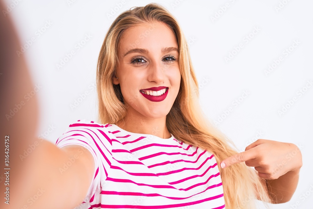 Beautiful woman wearing striped t-shirt make selfie by camera over isolated white background with surprise face pointing finger to himself Beautiful woman wearing striped t-shirt make selfie by camera over isolated white background with surprise face pointing finger to himself