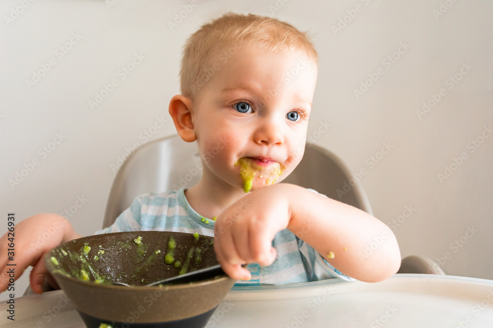Little boy alone eats puree from a plate. Little boy alone eats puree from a plate.