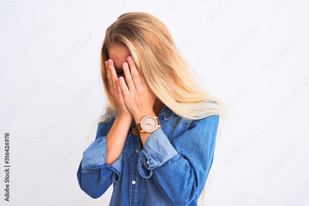 Young beautiful woman wearing casual denim shirt standing over isolated white background with sad expression covering face with hands while crying. Depression concept. Young beautiful woman wearing casual denim shirt standing over isolated white background with sad expression covering face with hands while crying. Depression concept.