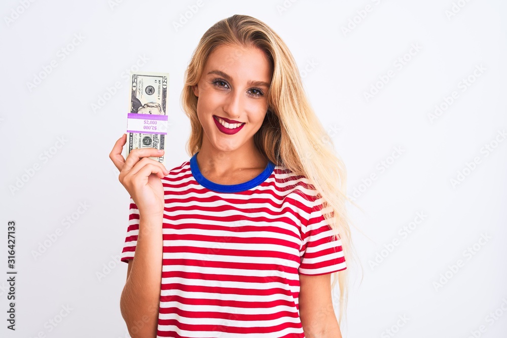 Beautiful woman wearing red striped t-shirt holding dollars over isolated white background with a happy face standing and smiling with a confident smile showing teeth Beautiful woman wearing red striped t-shirt holding dollars over isolated white background with a happy face standing and smiling with a confident smile showing teeth