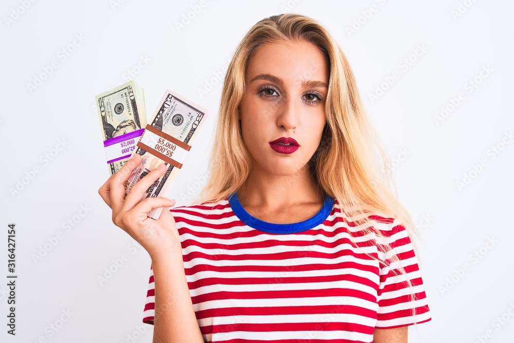 Beautiful woman wearing red striped t-shirt holding dollars over isolated white background with a confident expression on smart face thinking serious Beautiful woman wearing red striped t-shirt holding dollars over isolated white background with a confident expression on smart face thinking serious