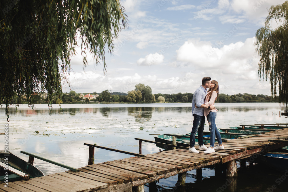 Young romantic couple is having fun in summer sunny day near the lake. Enjoying spending time together in holiday. Man and woman are hugging and kissing. Young romantic couple is having fun in summer sunny day near the lake. Enjoying spending time together in holiday. Man and woman are hugging and kissing.