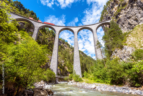 Landwasser Viaduct, Switzerland. Red train runs on high railroad bridge in mountains. This place is landmark of Swiss Alps. Scenic view of famous railway. photo