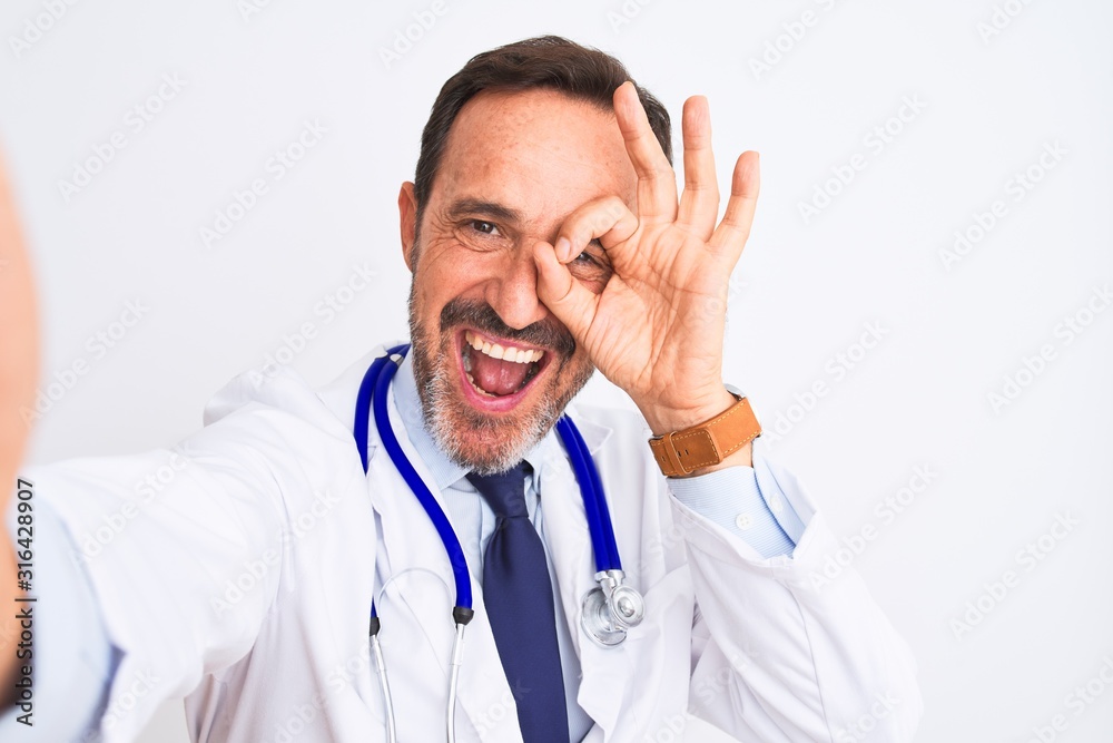 Middle age doctor man wearing stethoscope make selfie over isolated white background with happy face smiling doing ok sign with hand on eye looking through fingers Middle age doctor man wearing stethoscope make selfie over isolated white background with happy face smiling doing ok sign with hand on eye looking through fingers