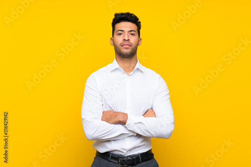 Young handsome man over isolated yellow background keeping arms crossed