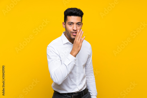 Young handsome man over isolated yellow background whispering something